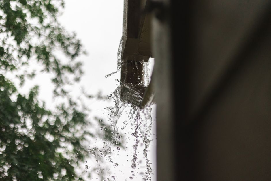 Water overflowing from a clogged gutter and running down the side of a house